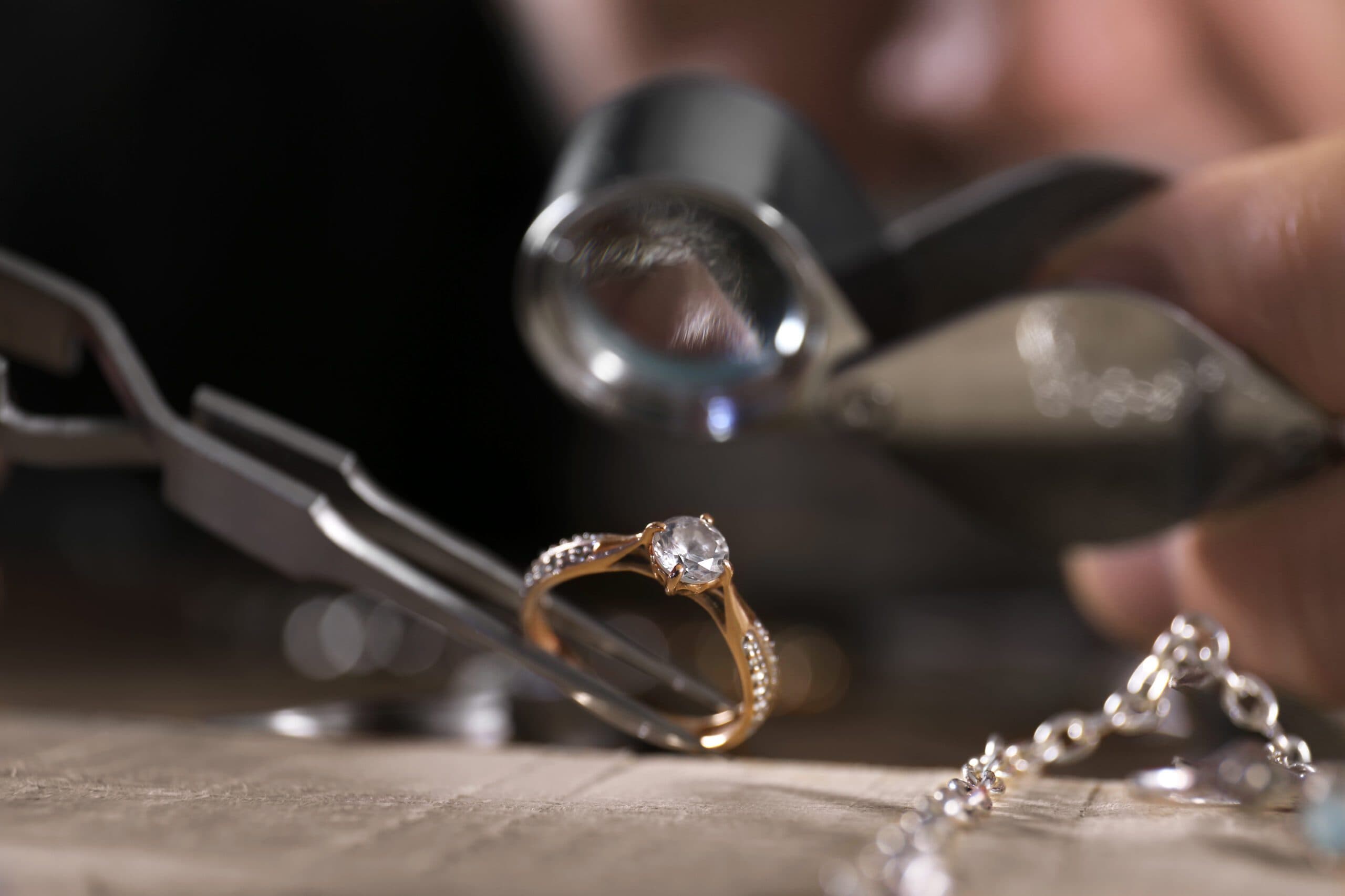 Gold diamond solitaire ring on workbench beside jeweler's pliers and loupe