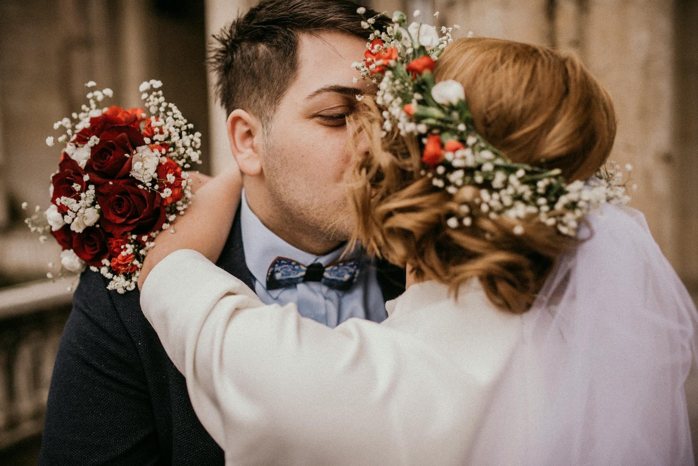 Bride and groom sharing a kiss, bride holding red roses and baby's breath bouquet
