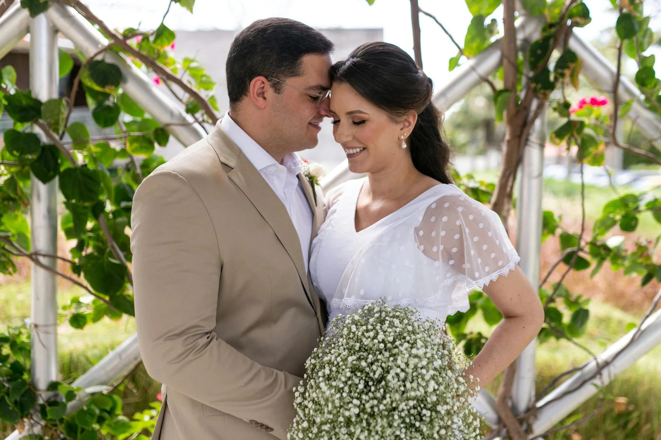Bride and groom touching foreheads tenderly, bride holding large baby's breath bouquet outdoors