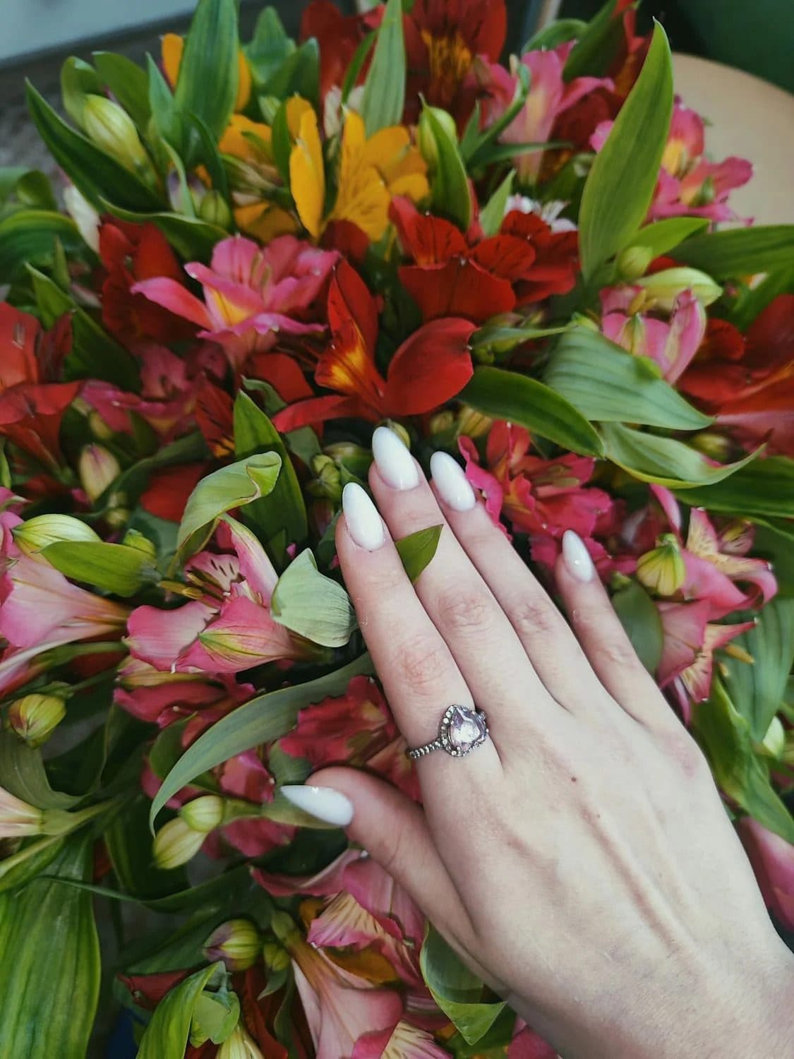 Hand with white almond nails wearing a silver halo ring resting on colorful alstroemeria bouquet
