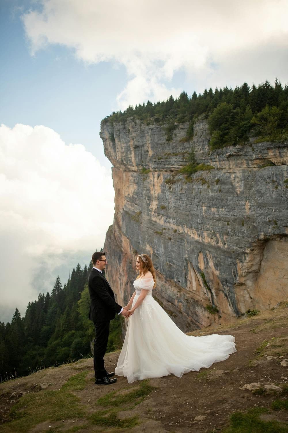Bride and groom holding hands on a mountain cliff edge with dramatic rocky backdrop