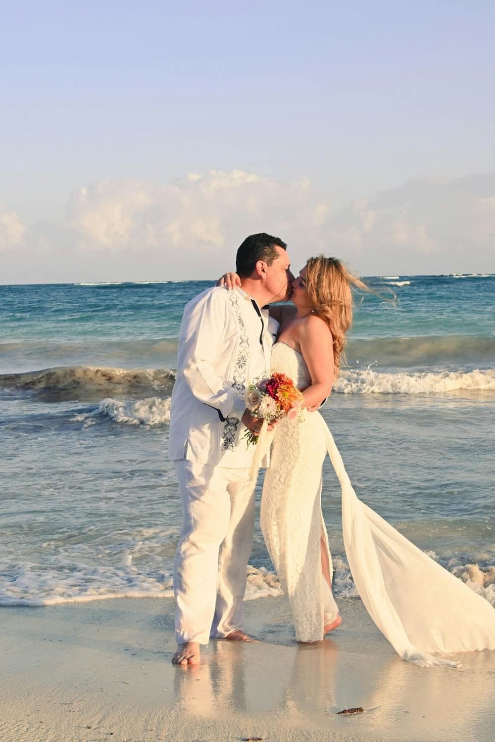 Bride and groom kissing barefoot on a tropical beach with turquoise waves