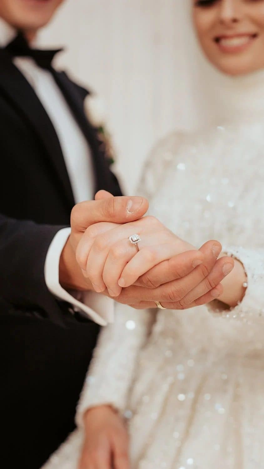 Bride and groom holding hands showing a diamond halo engagement ring on her finger