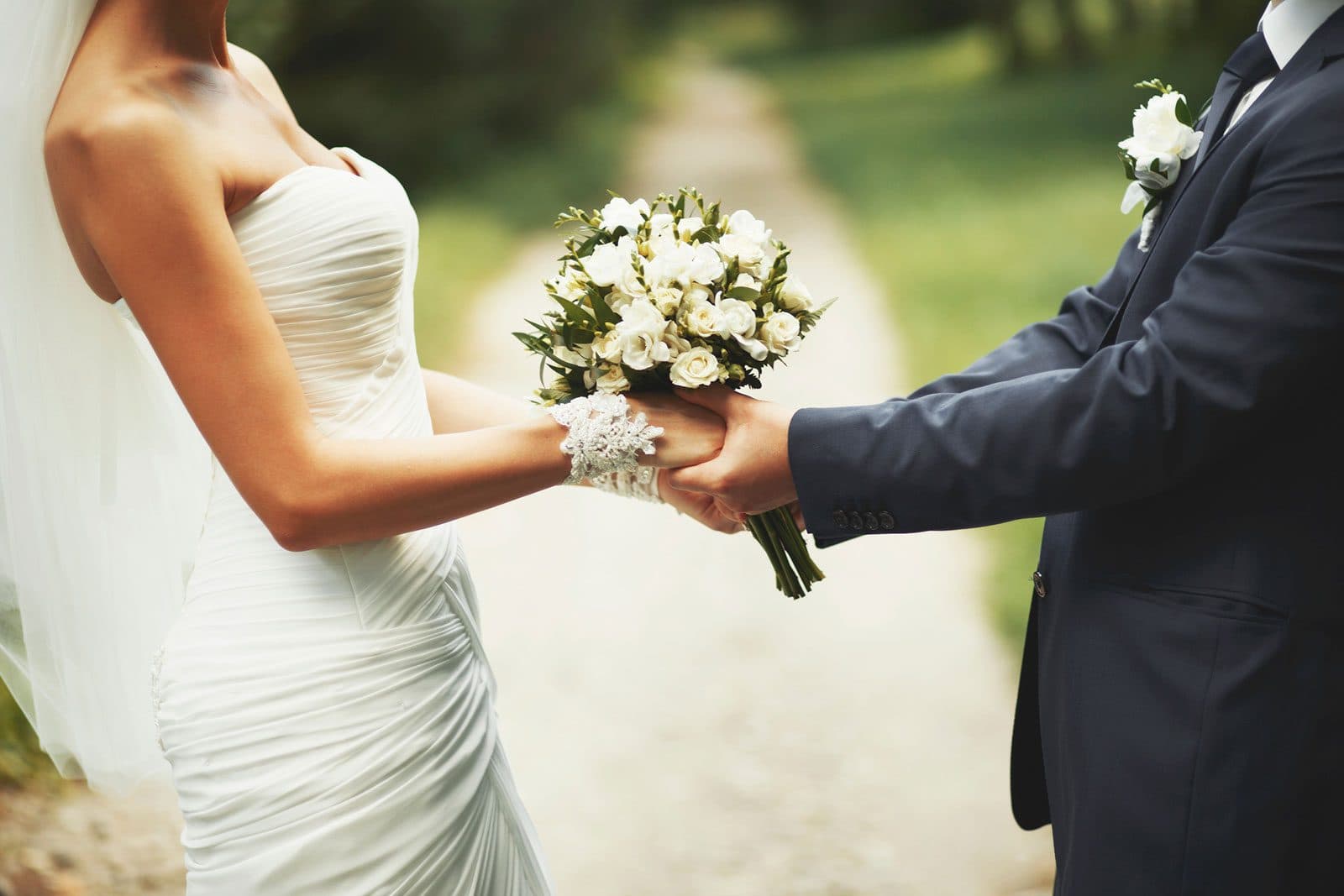Bride in strapless white gown and groom in navy suit holding white rose bouquet outdoors