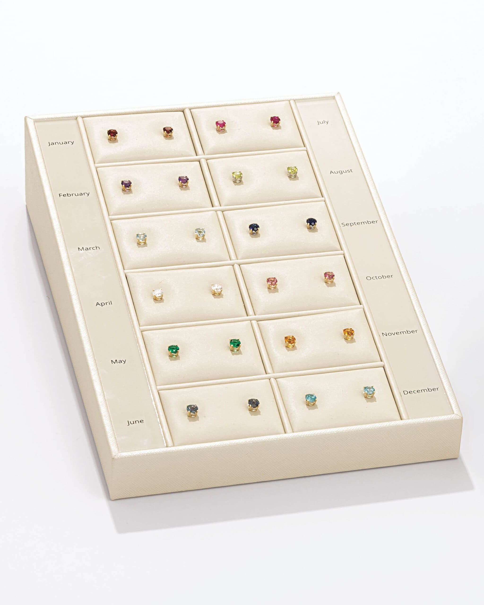 Cream display tray showing twelve pairs of birthstone stud earrings labeled by month
