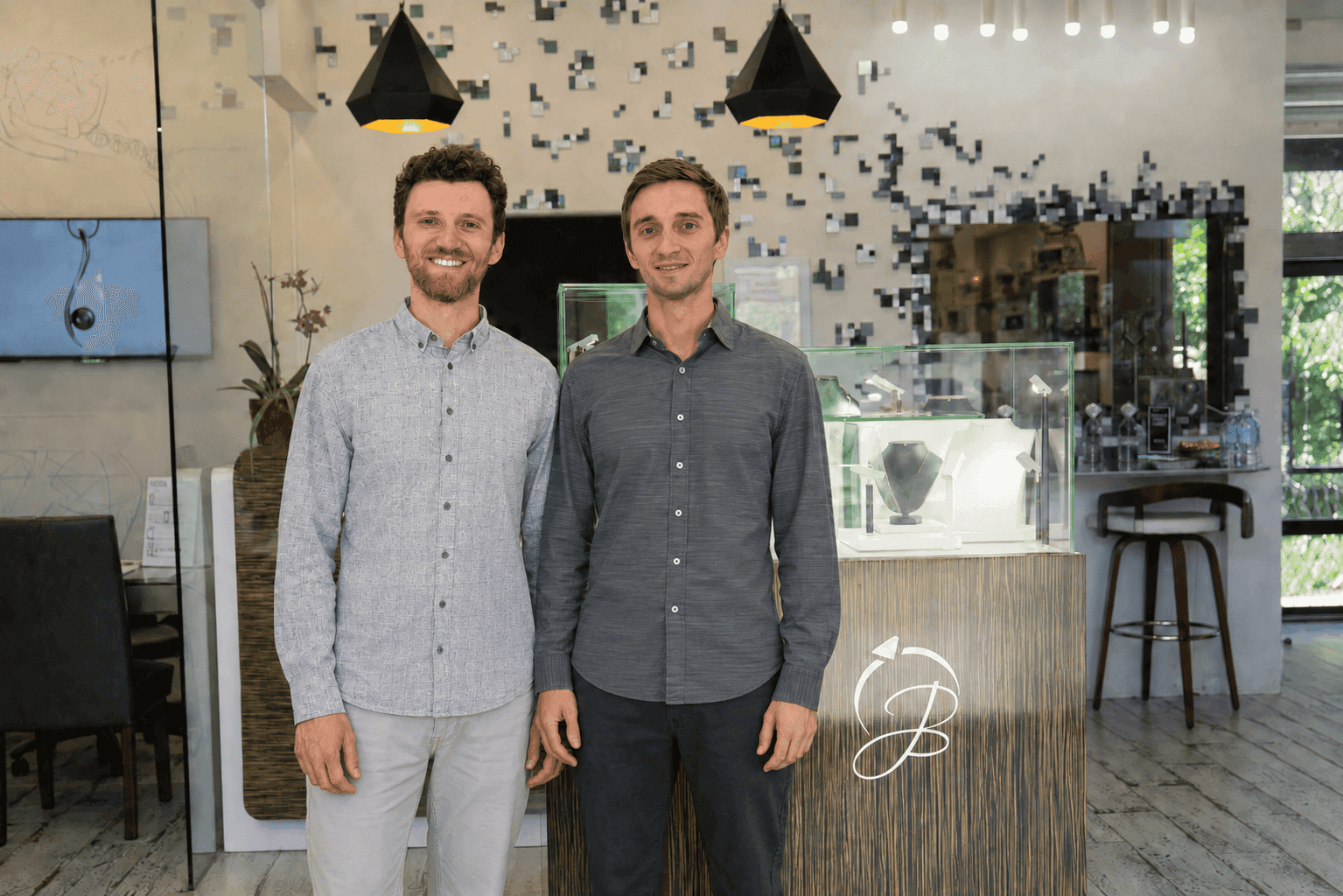 Two smiling men standing together in front of a jewelry store display counter
