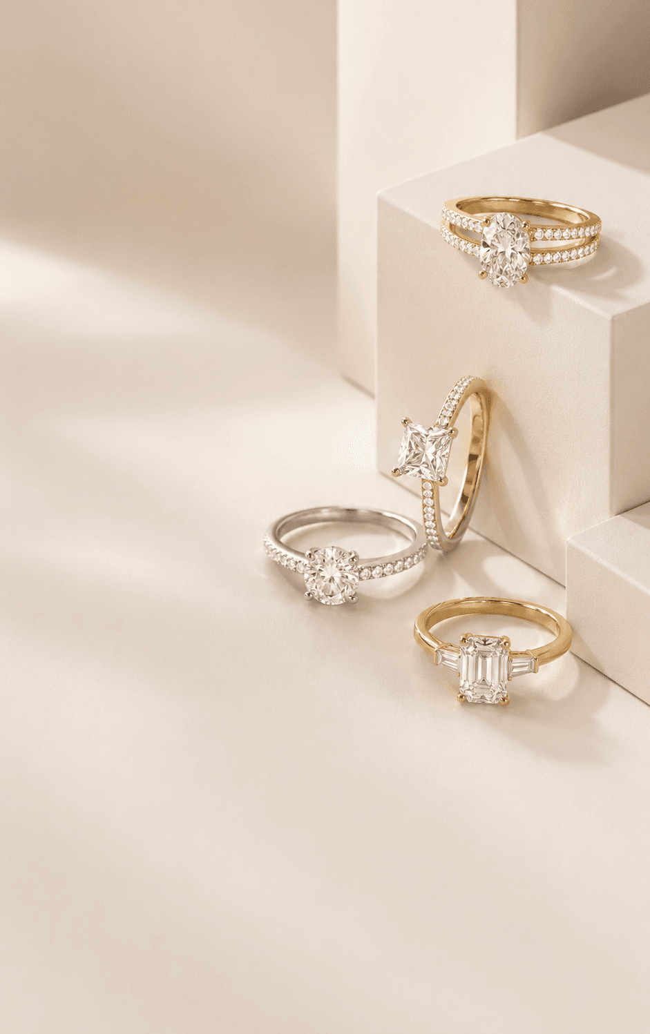 Four diamond engagement rings in yellow gold, rose gold, and white gold on cream pedestals