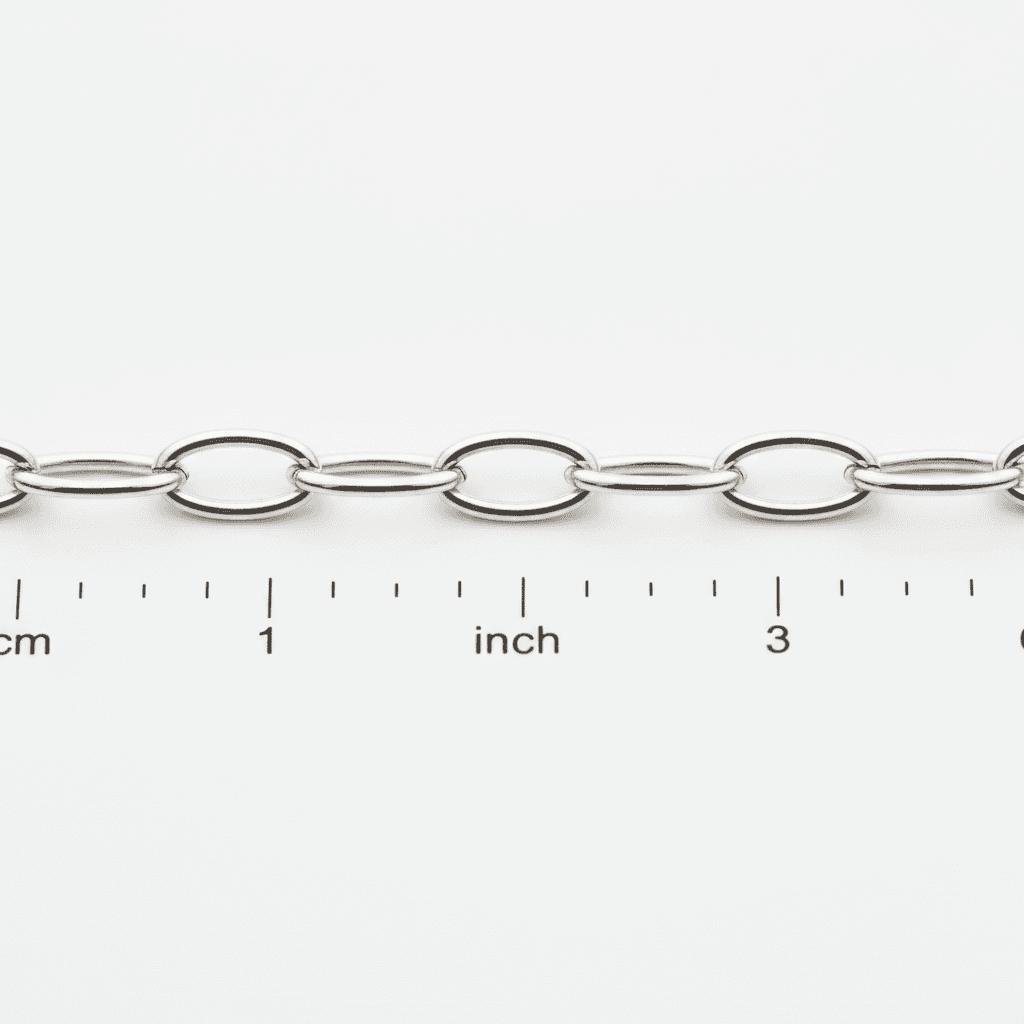 Close-up of a polished silver oval cable chain against a ruler showing scale