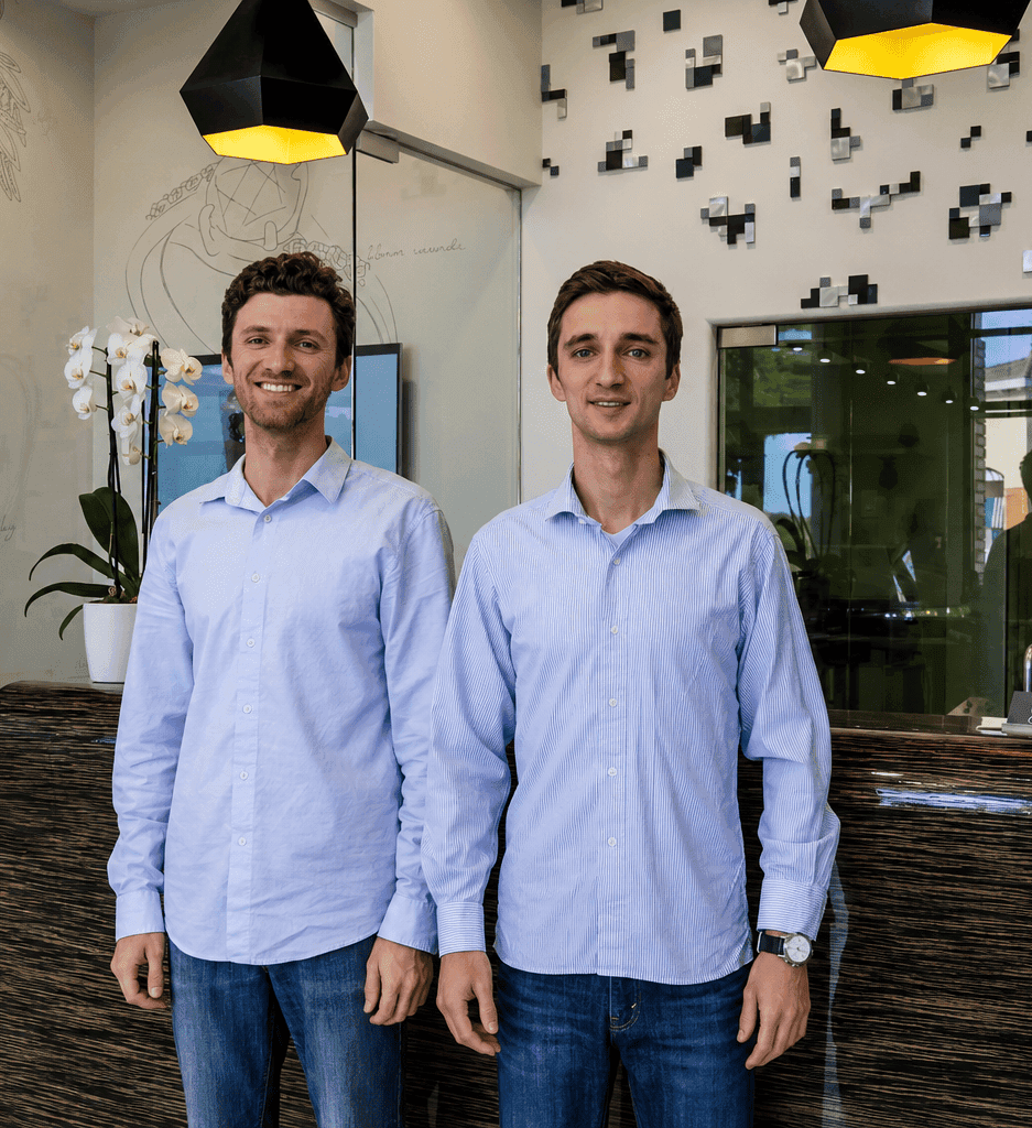 Two smiling men in light blue shirts standing at a jewelry store reception counter