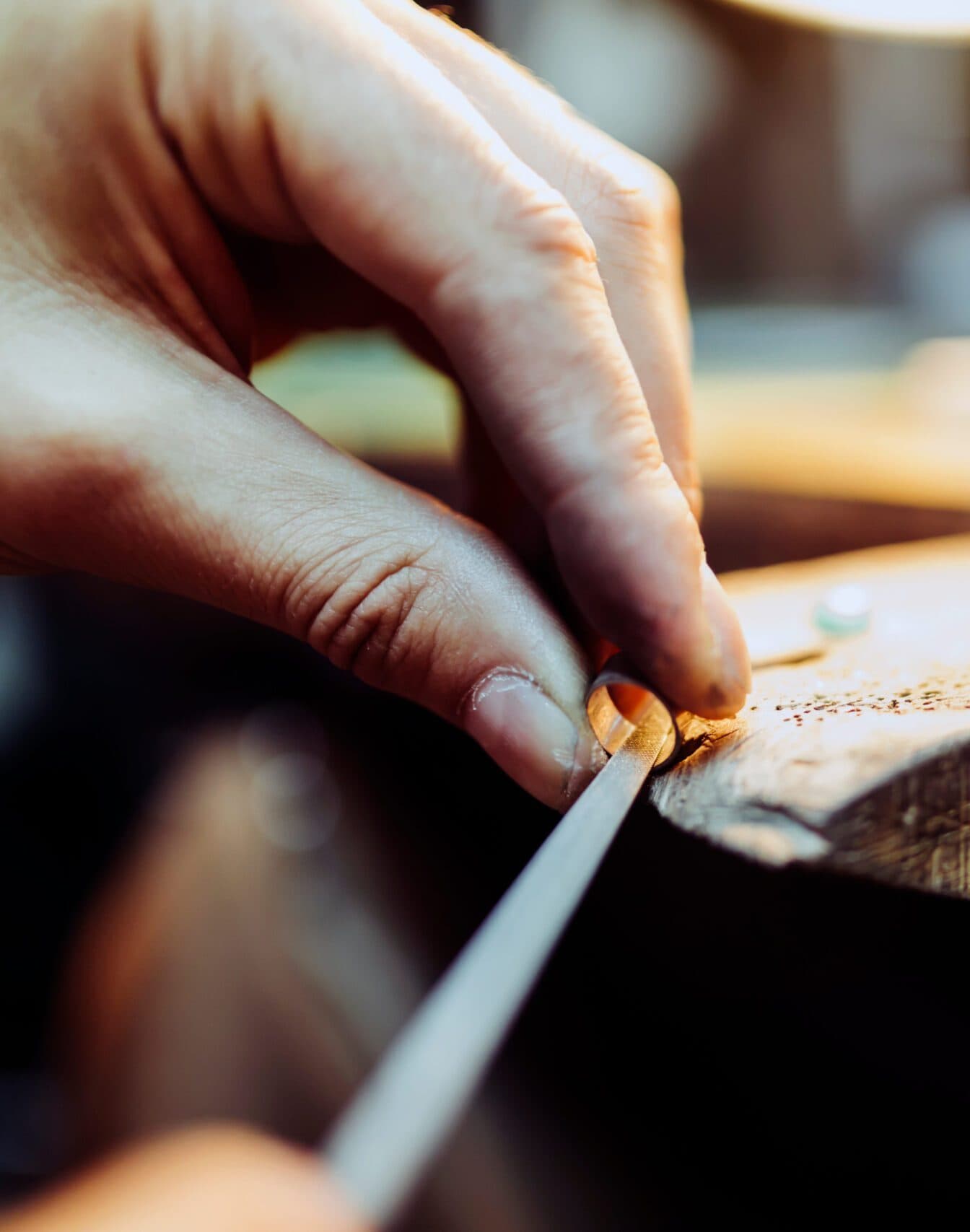 Jeweler's hands filing a gold ring on a wooden workbench