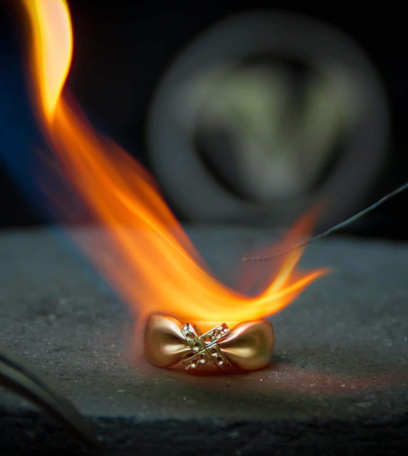 Jeweler soldering a gold ring with a torch flame on a stone block