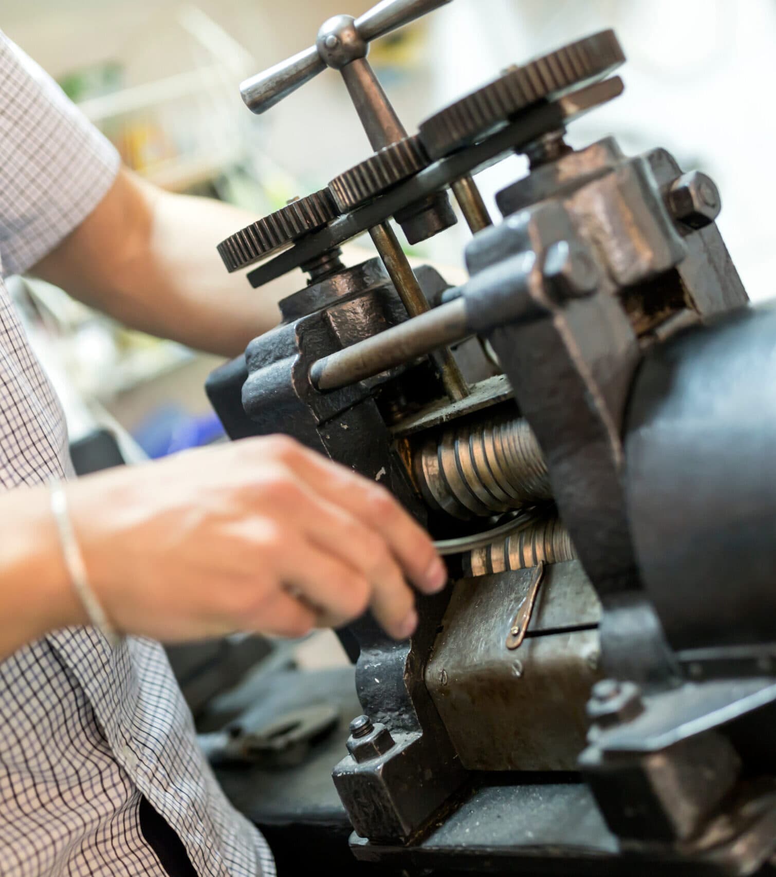 Goldsmith's hands feeding metal sheet through a heavy cast-iron rolling mill