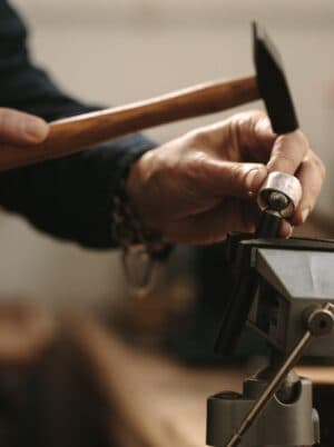 Jeweller's hands using a hammer and punch to set a stone in a bench vise