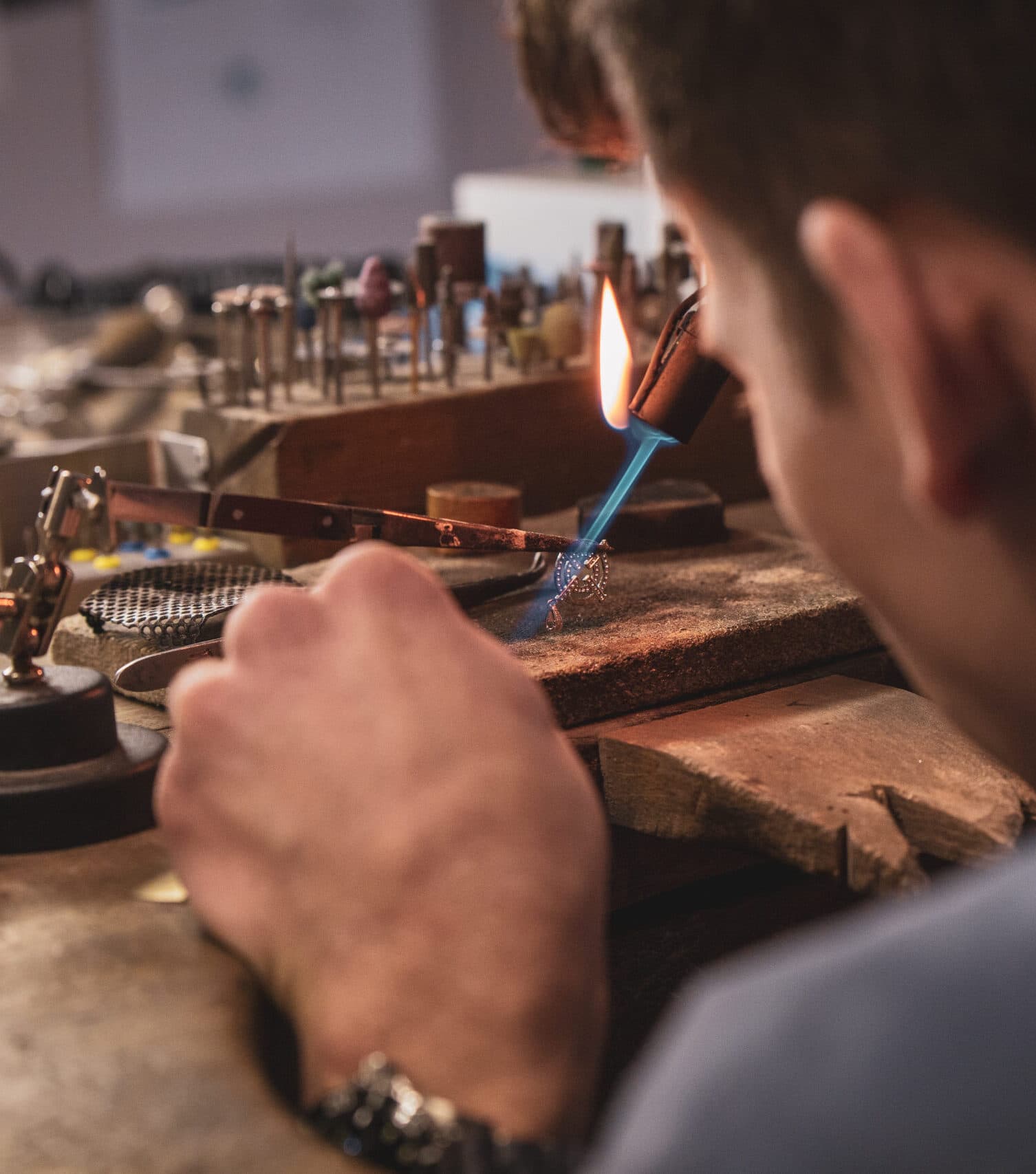 Jeweller soldering a delicate piece with a blue-flame blowpipe at a wooden workbench
