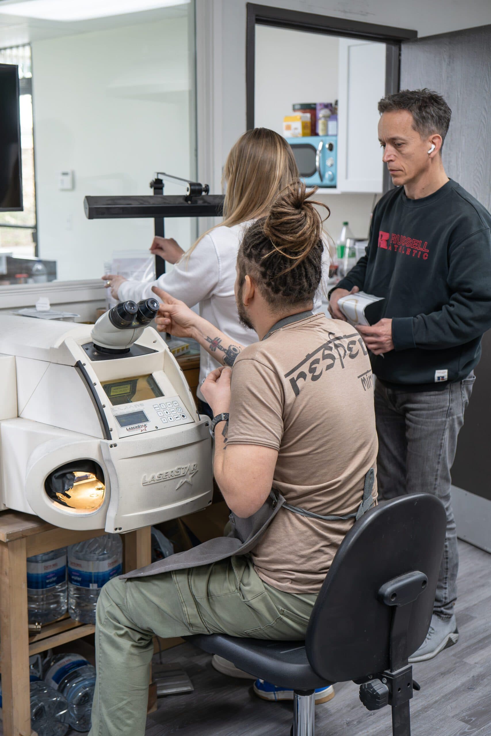 Three jewellers working around a LaserStar laser welding machine in a workshop