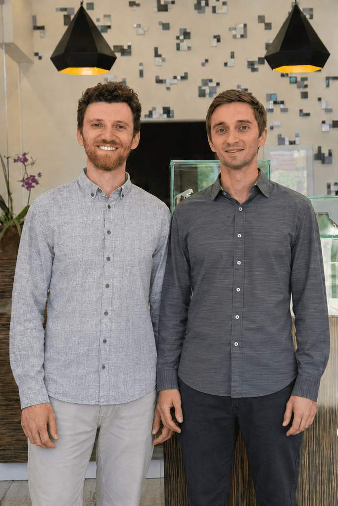 Two smiling men in grey button-up shirts standing together indoors
