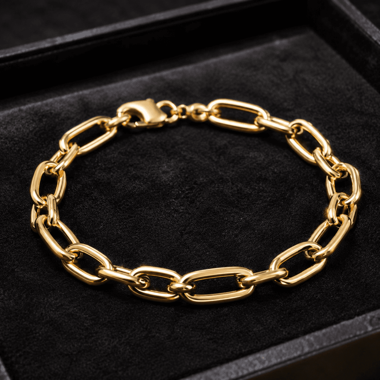 A close-up of an elegant yellow gold link bracelet laid flat on a dark velvet tray, warm directional lighting highlighting