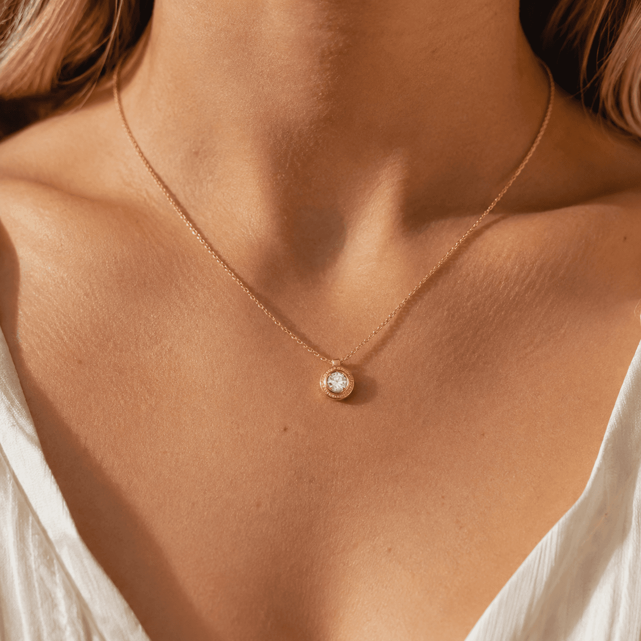 A close-up of a woman's neckline showing a perfectly fitted gold pendant necklace resting at the collarbone, warm natural