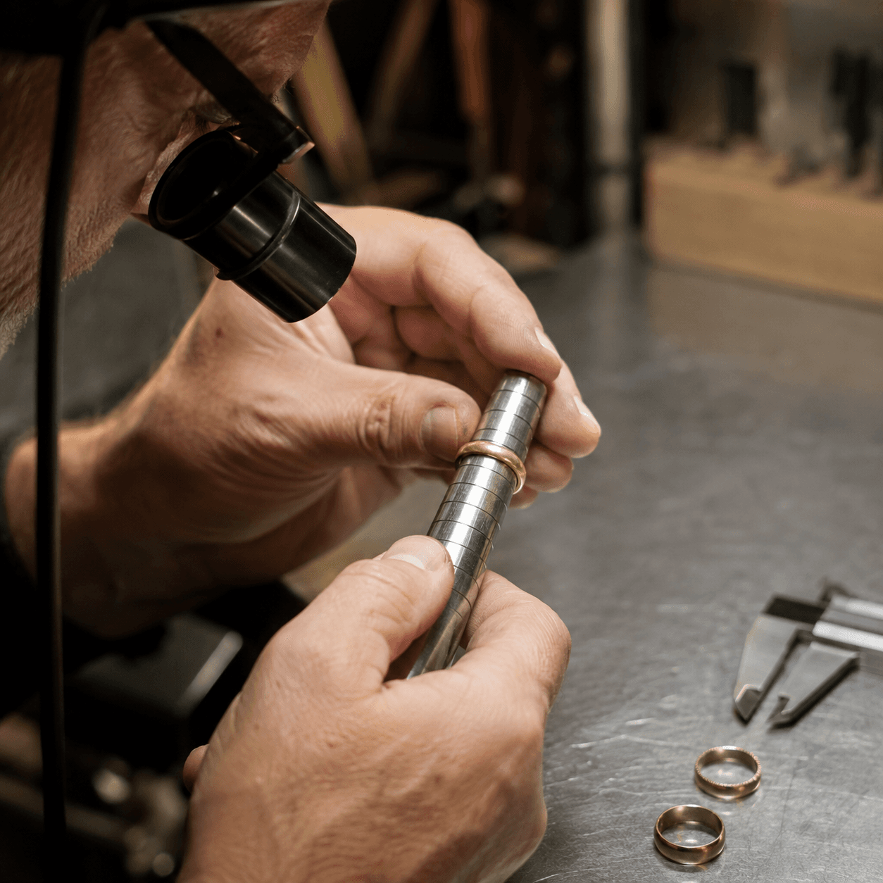 A skilled jeweler using a ring mandrel to resize a gold band on a polished steel workbench, close-up shot, warm workshop